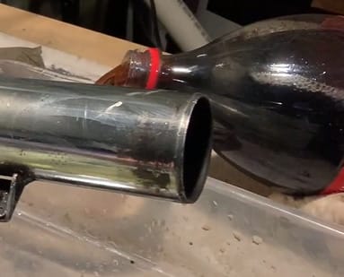 A bottle of soda is being poured into a metal pipe in an attempt to remove rust