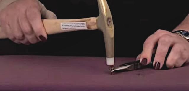 A person demonstrating how to use a tack hammer on a fabric
