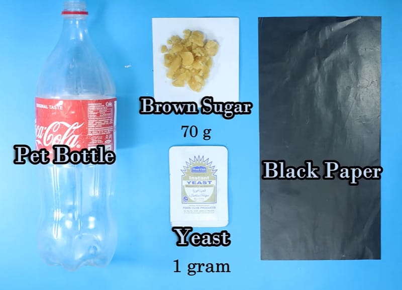 A pet bottle of coke, brown sugar, yeast ad black paper in a blue background