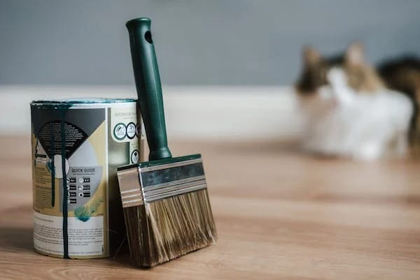 A can of paint and brush on a wooden floor
