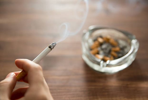 At home, a person calmly smokes a cigarette on a wooden table