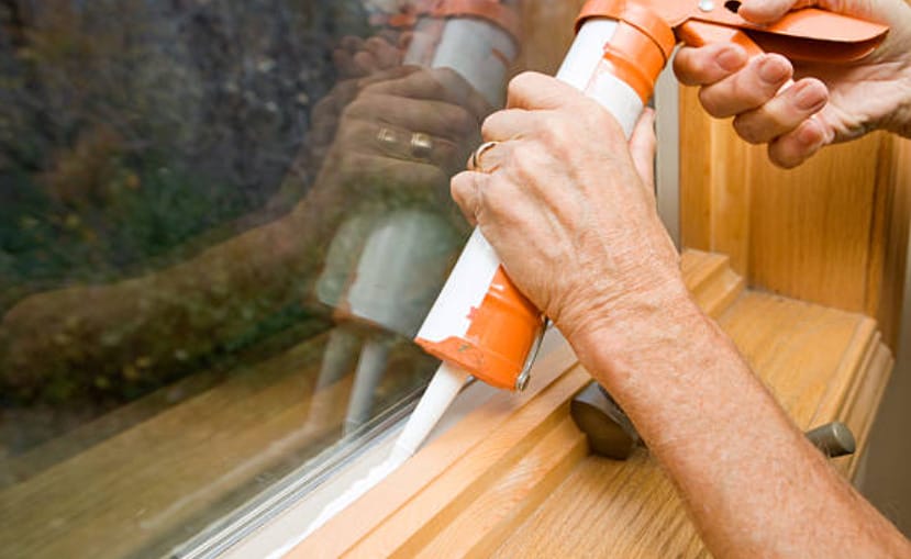 A woman using sealant to seal window gaps