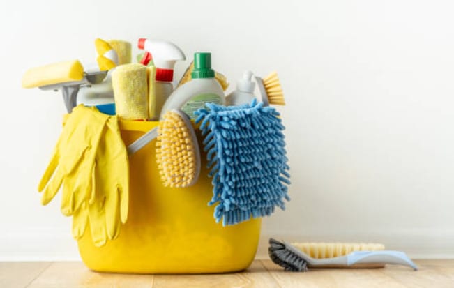 A cleaning tool and materials on a yellow pail with two brushes on the wooded floor