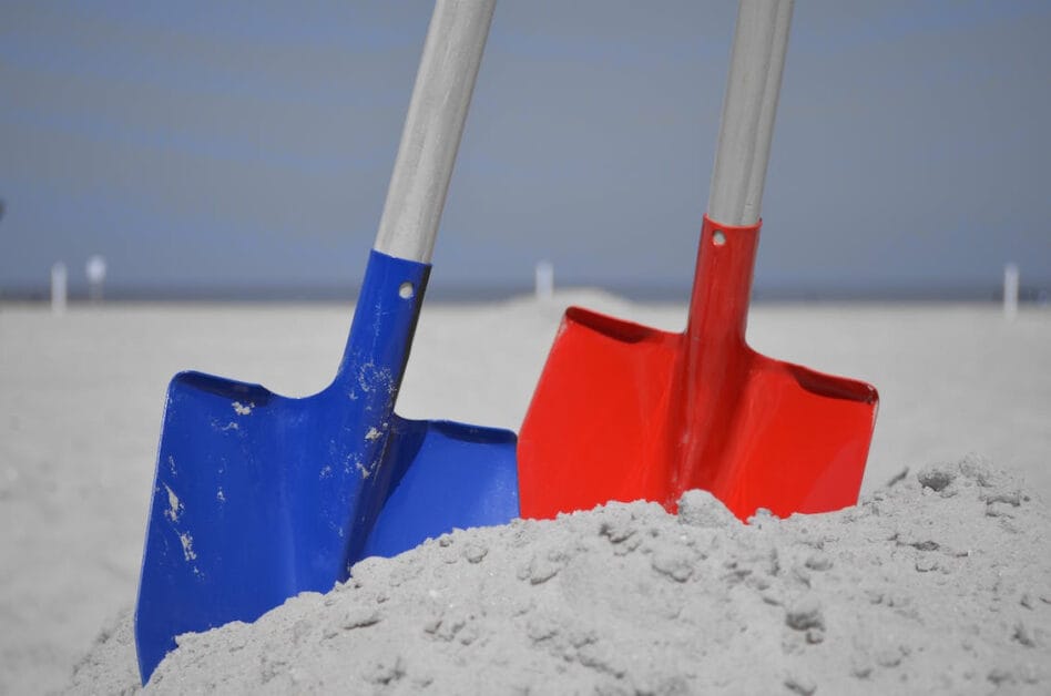 A blue and red shovel on the beach sand