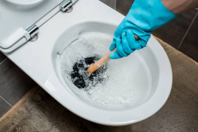 A person wearing blue cleaning gloves plunging the clog toilet