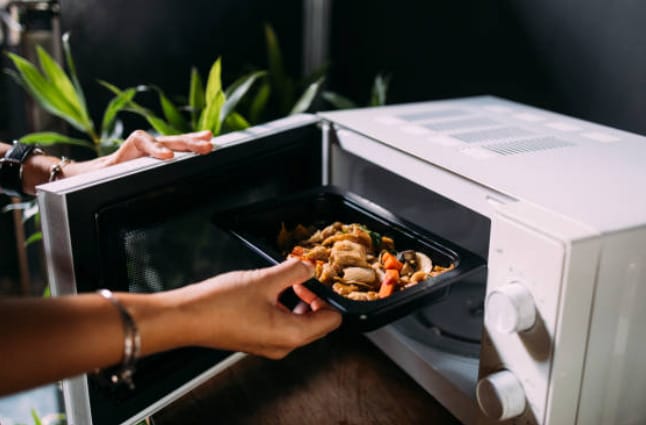 A person putting food into a microwave oven