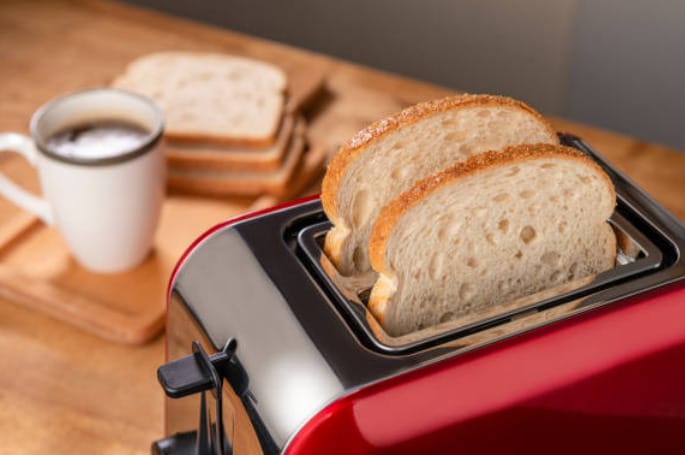 A red toaster with sliced bread on it white a coffee and sandwich on the background