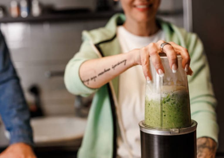 A woman is making a green smoothie in a blender