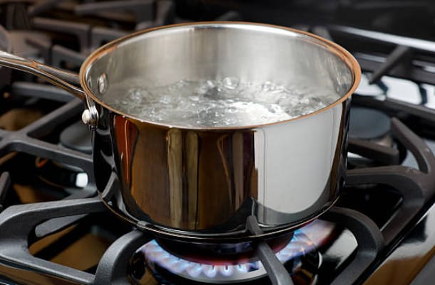 A pot of boiling water on top of a fired stove