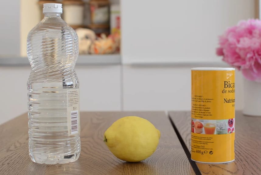 A bottle of sparkling water next to a lemon and baking soda on a table