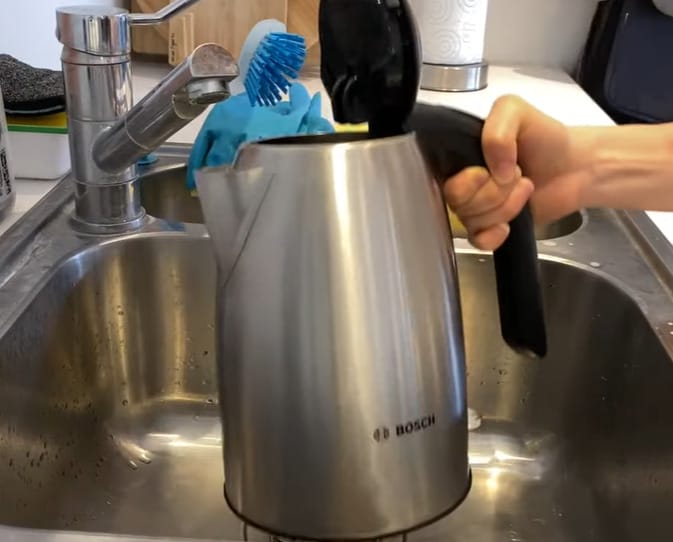 A person holding a BOSCH electric kettle on the kitchen sink
