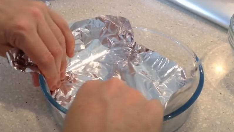 A person adding aluminum foil to a glass bowl