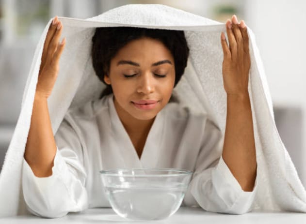A woman with a towel covering her head and breathing on a bowl of hot water