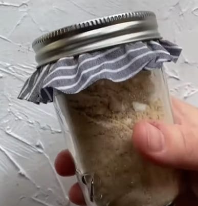 A person holding a small jar of a mixture of baking soda, essential oil, and rosemary powder