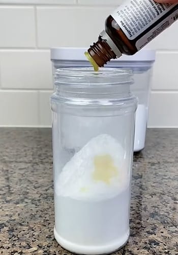 A person pouring an essential oil into a small jar of baking soda powder