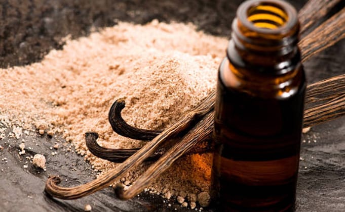 A bottle of vanilla essence, a cinnamon powder and stick on a wooden table