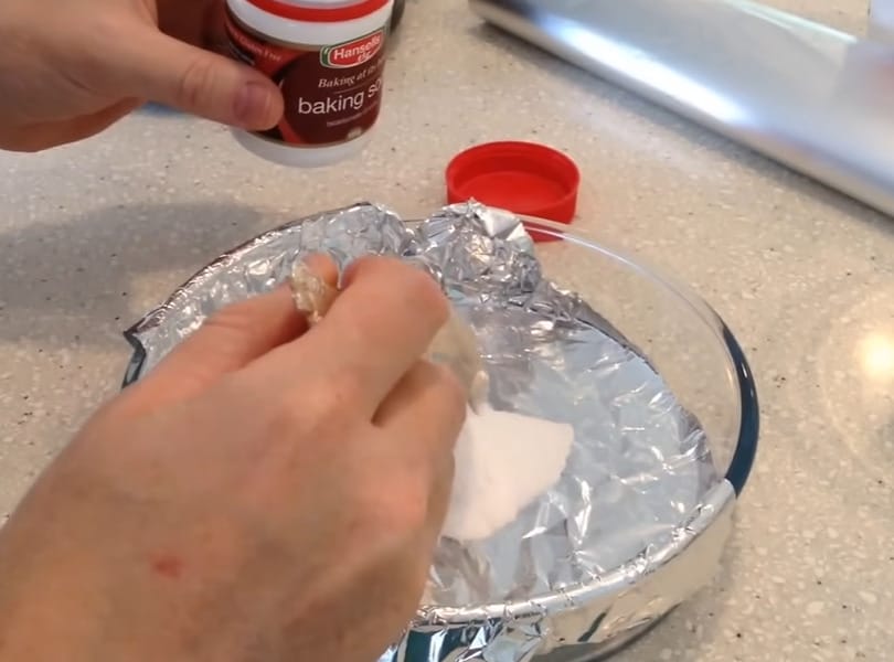 A person is putting a baking soda into a bowl wrapped with aluminum foil