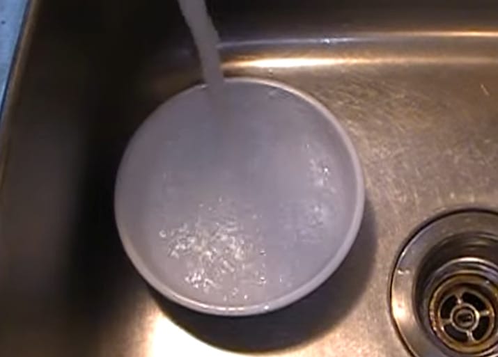 A bowl of boiling water is being poured into a sink