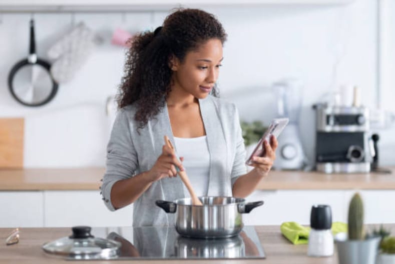 A woman multitasking on her phone while cooking in the kitchen