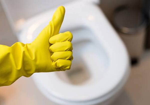 A person in a yellow rubber glove is giving a thumbs up in front of a toilet bowl