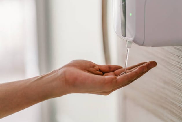 A person catching a liquid soap from automatic dispenser in a bathroom