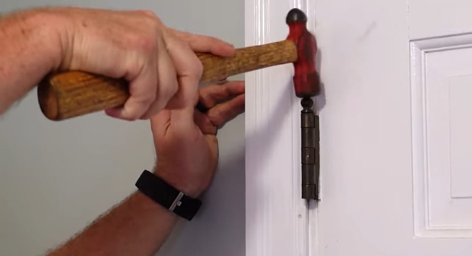 A person hammering the hinge pin on the door