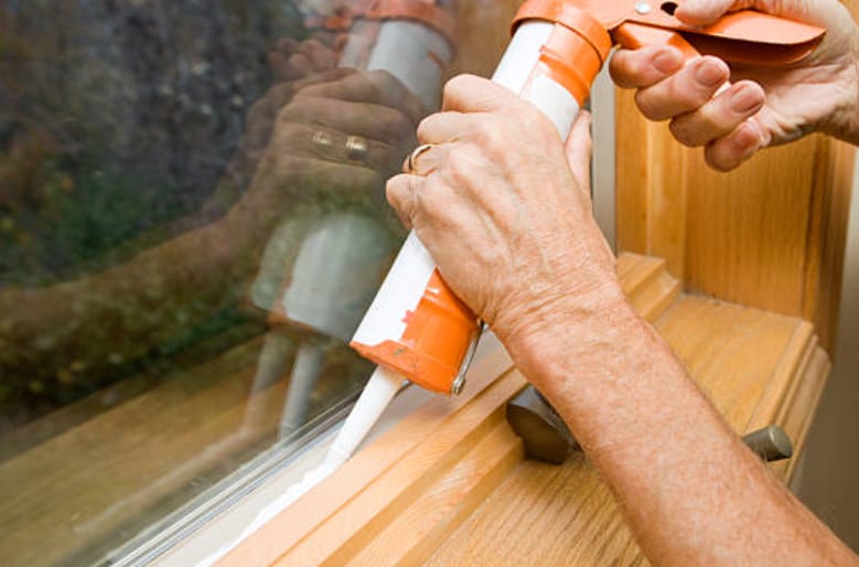 A woman is using a tool to apply a sealant to a window with gaps