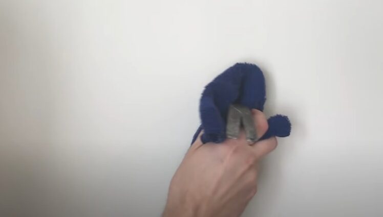A person using a blue clothe to cover the hammer and find a wall stud