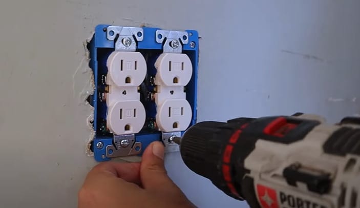A person is using a drill to install a double outlet on a wall
