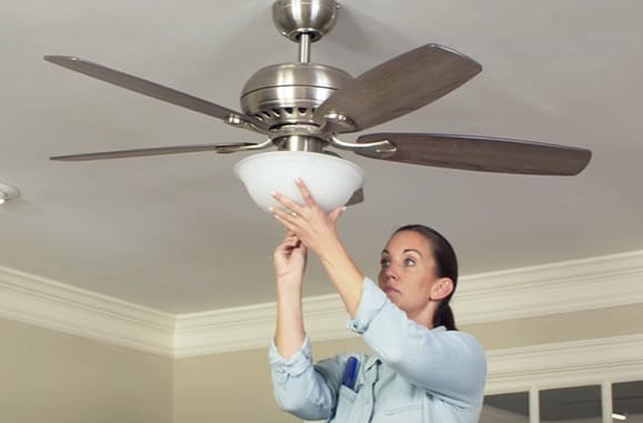 A woman installing a light on a ceiling fan 
