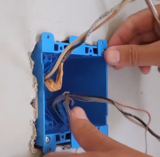 A person installing a blue electric box with wires in it