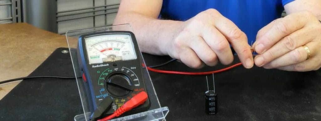 A person connecting the multimeter probes to the capacitor's terminals