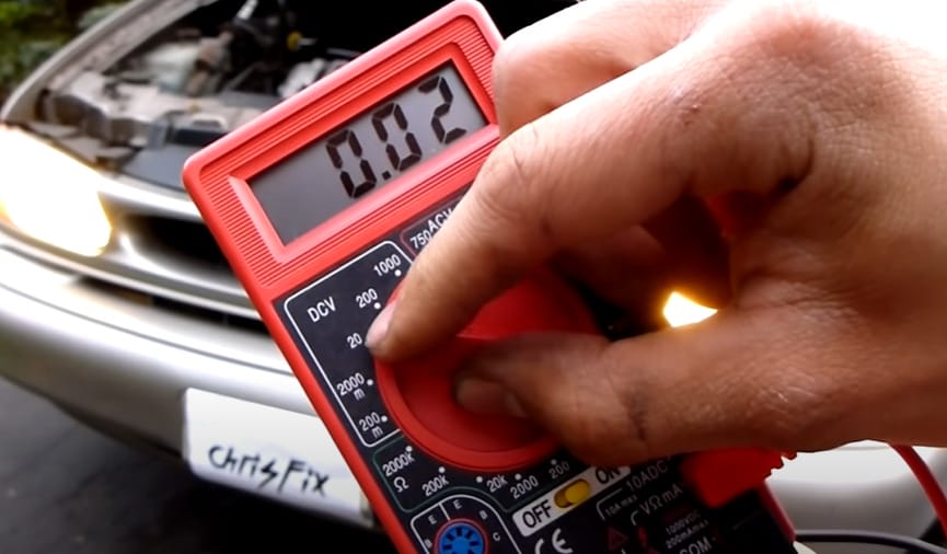 A person is holding a red multimeter with 0.02 reading