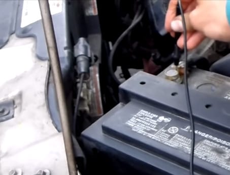 A person is using a multimeter to test a car battery