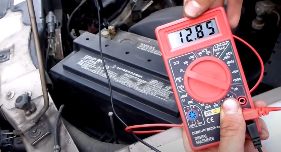 A person is holding a multimeter at 12.85 reading