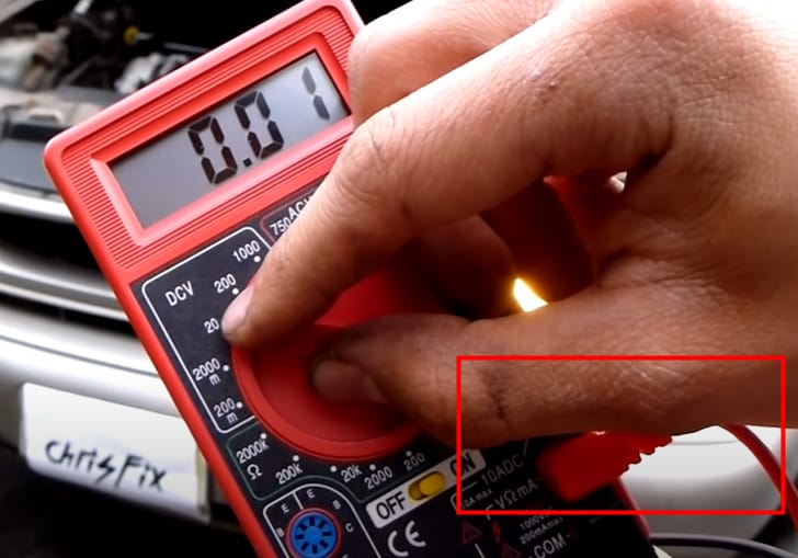 A person is holding a red multimeter at 0.01 reading