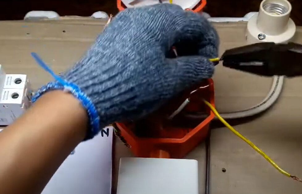A person wearing gray gloves is using pliers to connect wires in series to a box