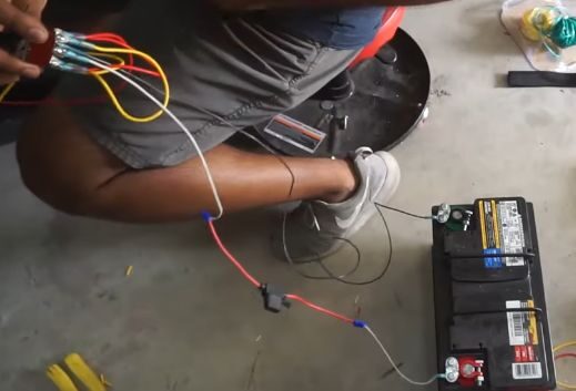 A man is working on a car battery to wire power windows to a toggle switch