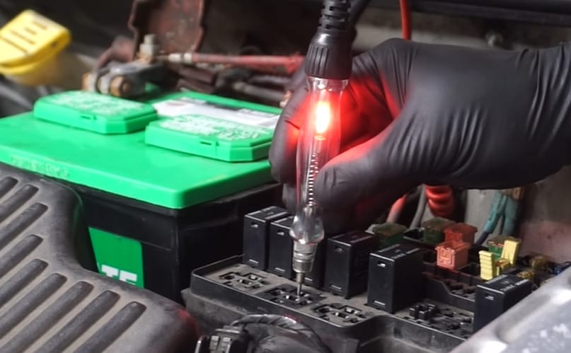 A person wearing a black gloves is using a test light to a car's relay
