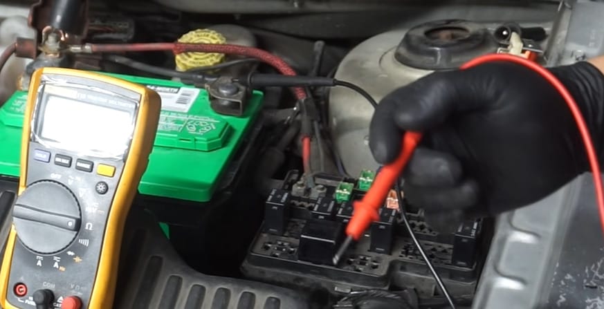 A person wearing a black gloves testing the relay of a car with a multimeter