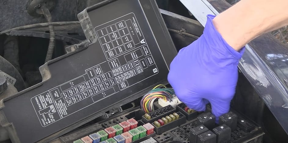 A person wearing a purple glove while working on a car's relay