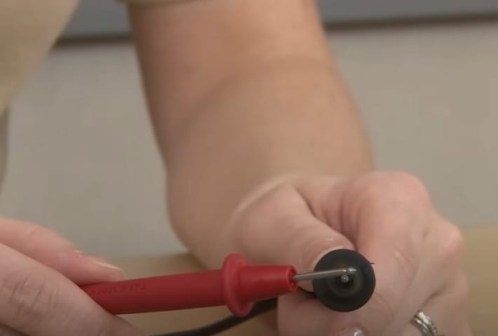 A person is holding a multimeter's red and black probe