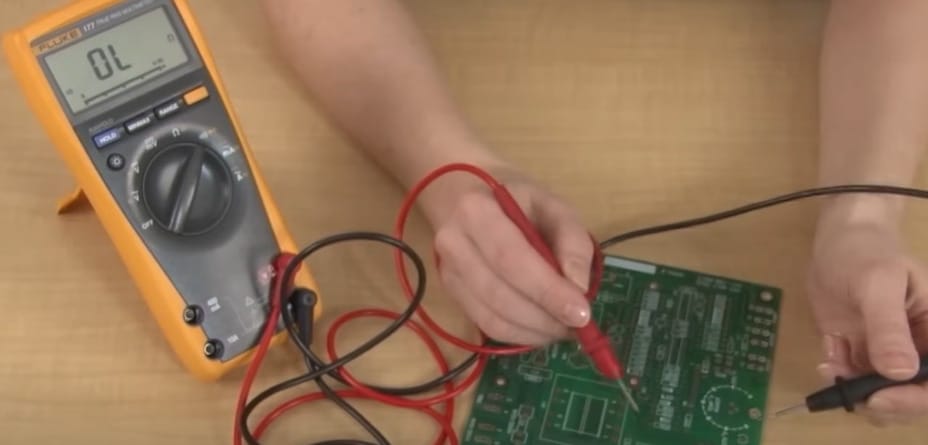 A person using a multimeter to check continuity on a circuit board
