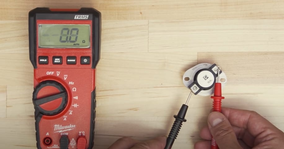 A person is testing the voltage of a device using a TRMS multimeter in red and black color