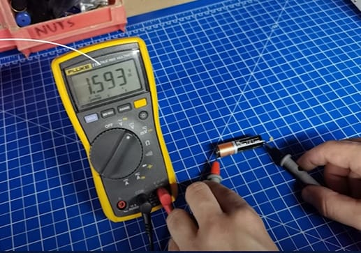 A person is using a multimeter in testing an AA Duracell battery