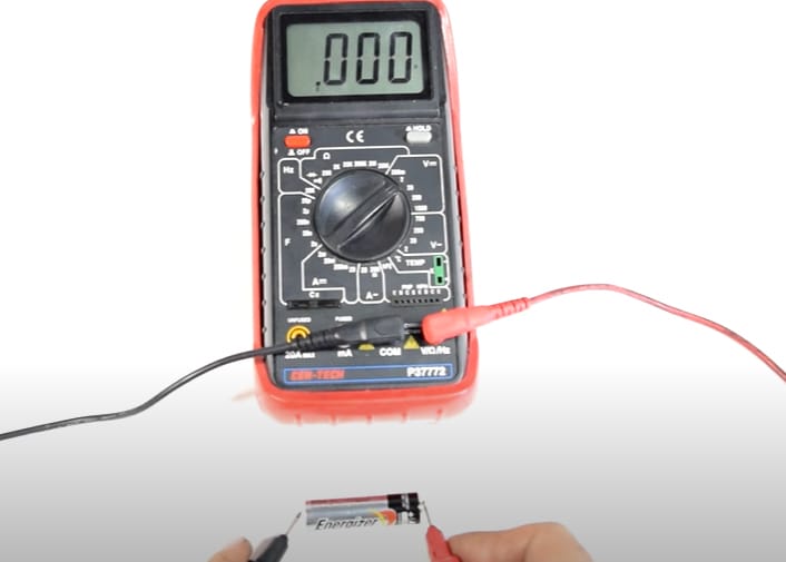 A multimeter at a 0.00 reading while a person is putting the multimeter's probe at the both ends of an AA battery