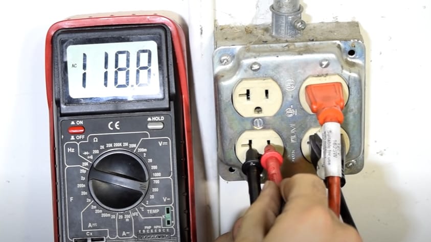 A person is testing an old outlet with a multimeter