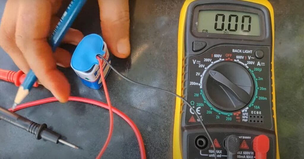 A person holding a pencil and a 12v battery to be tested by a multimeter