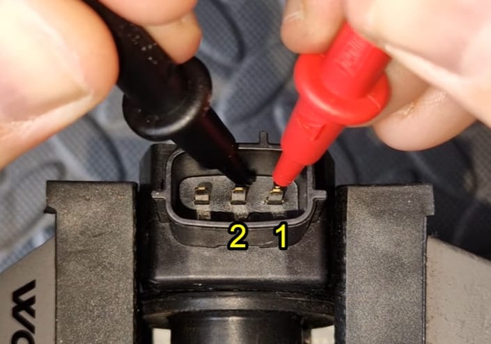 A person is connecting the black and red probe of a multimeter into the coil pack