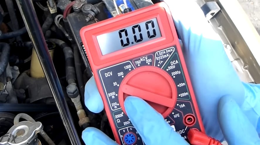 A person in a blue gloves using a multimeter to test the alternator of a car